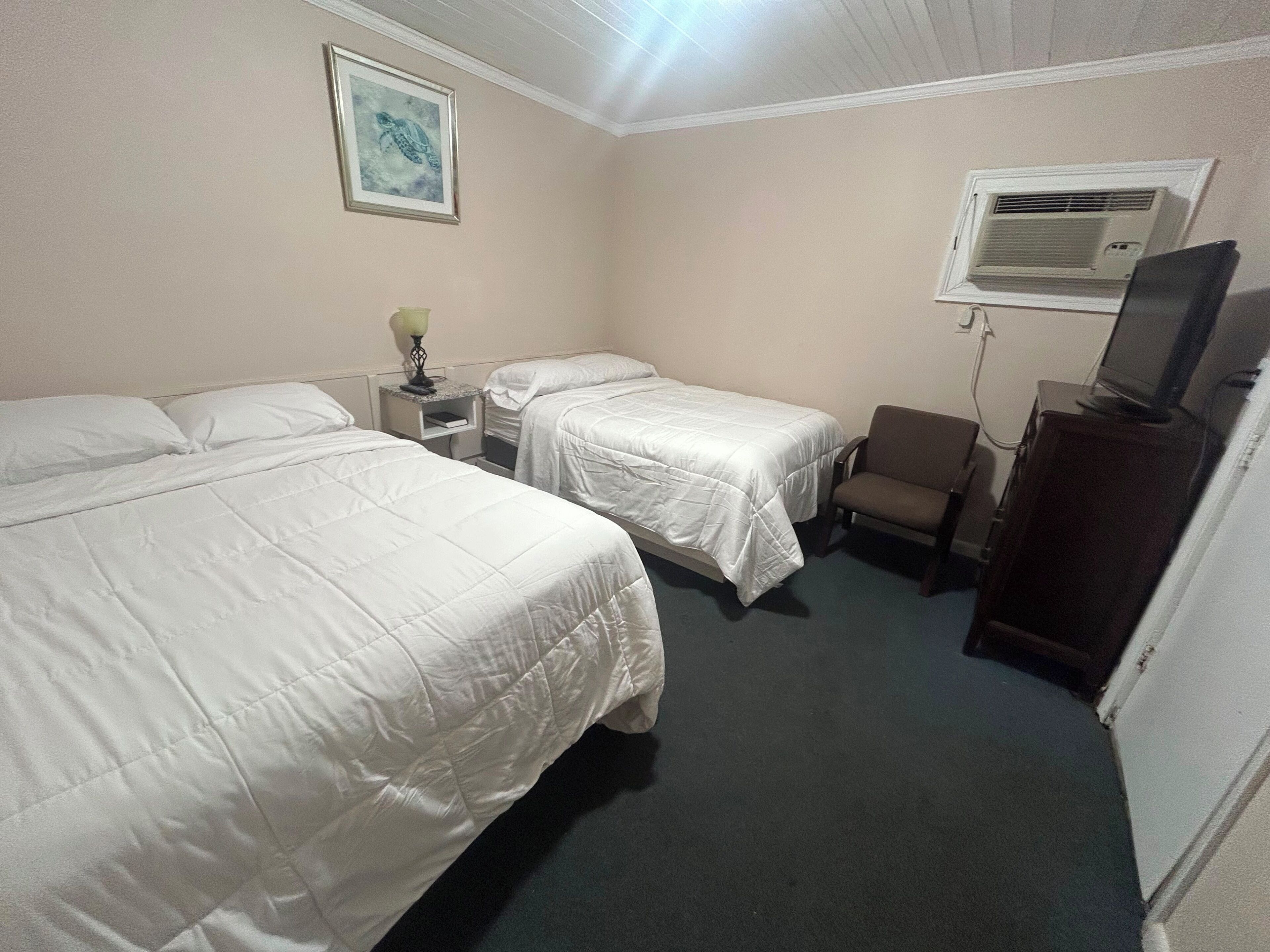 Une chambre d’hôtel avec deux lits, un bureau, une chaise, une télévision et un appareil de climatisation.