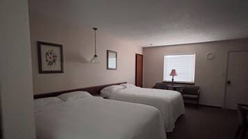 Habitación de hotel con dos camas, una mesita, una silla, una lámpara y una ventana con persianas.