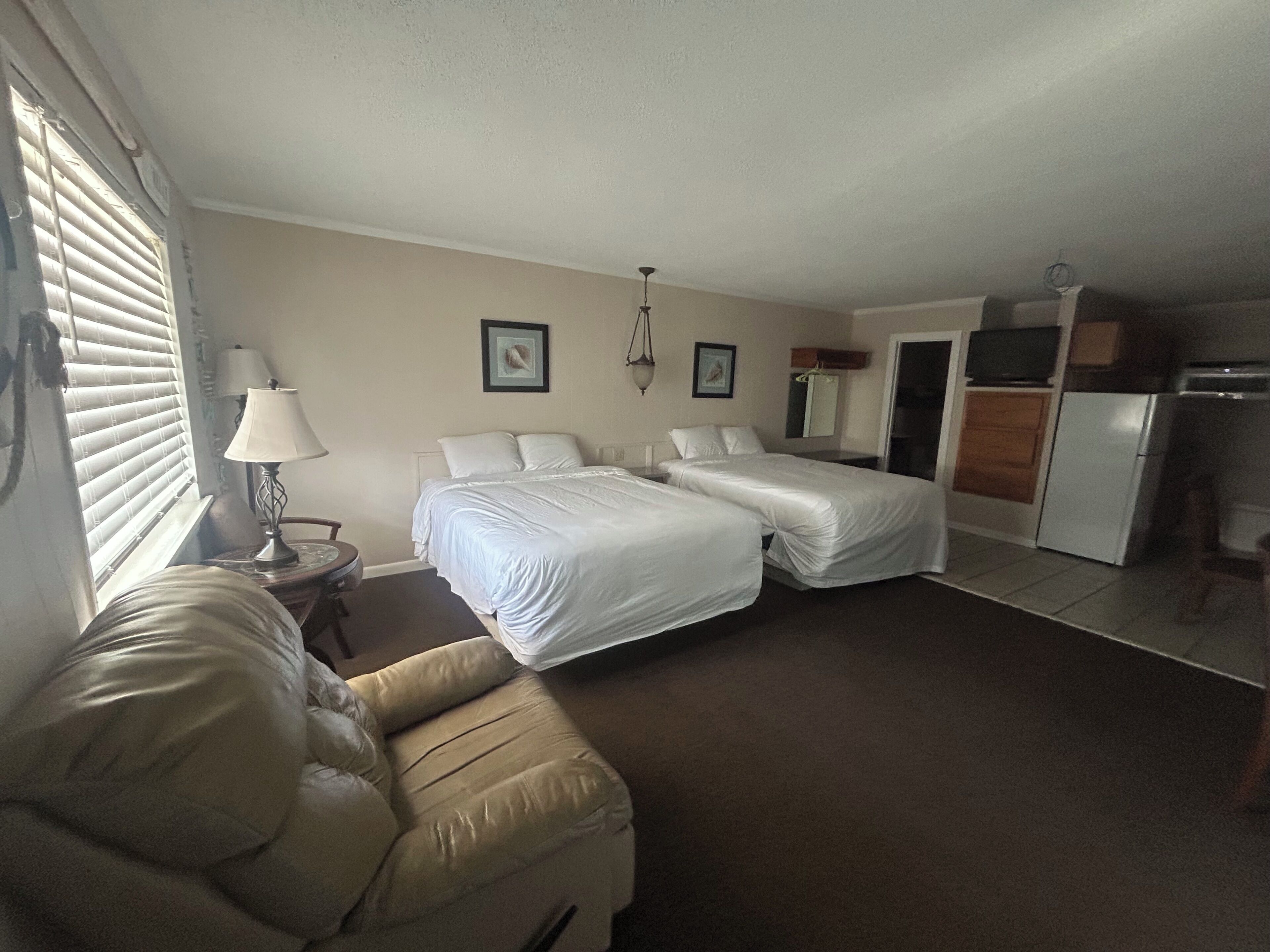 Une chambre d’hôtel avec deux lits, un canapé, un bureau, une lampe et une kitchenette.