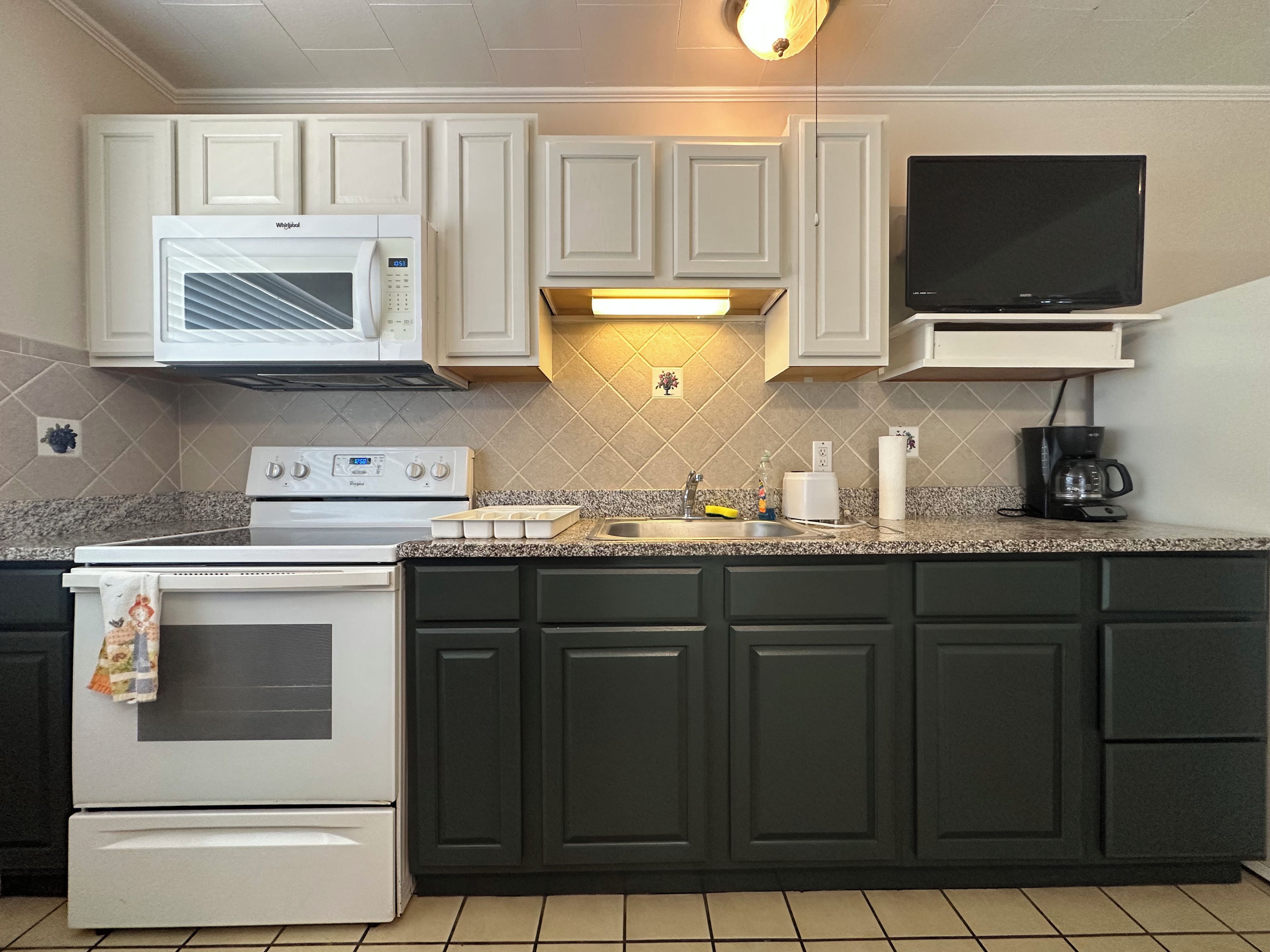 A kitchen with white cabinets, a microwave, a stove, a sink, and a coffee maker.