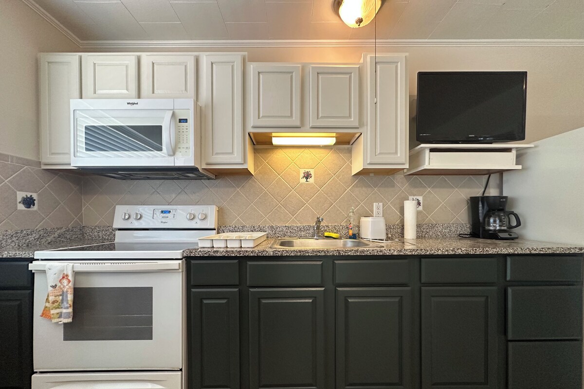 A kitchen with white cabinets, a microwave, a stove, a sink, and a coffee maker.