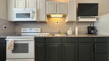 A kitchen with white cabinets, a microwave, a stove, a sink, and a coffee maker.