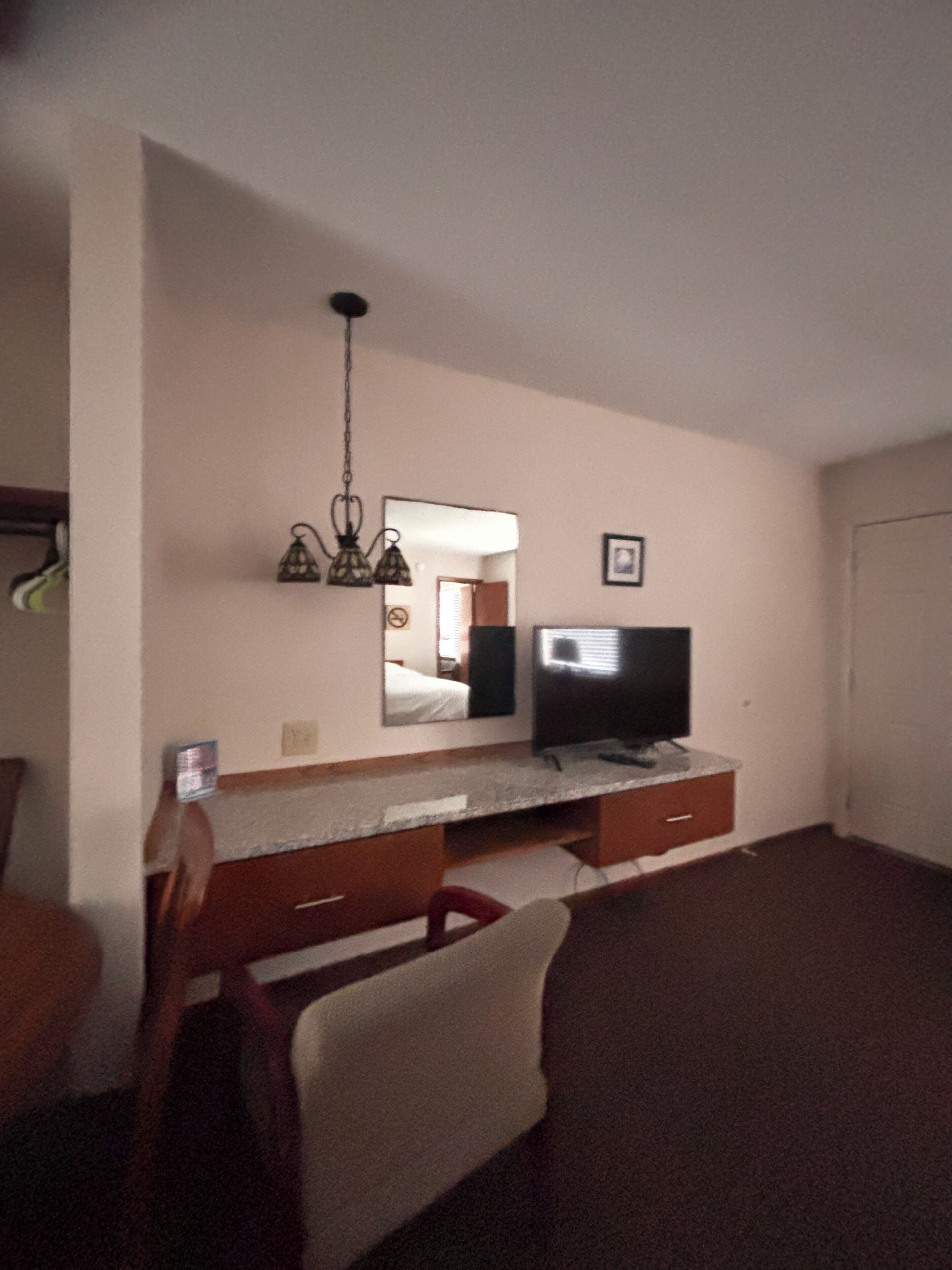 Ein Zimmer mit einem Holztisch, einem Fernseher, einem Spiegel und einer Pendelleuchte.