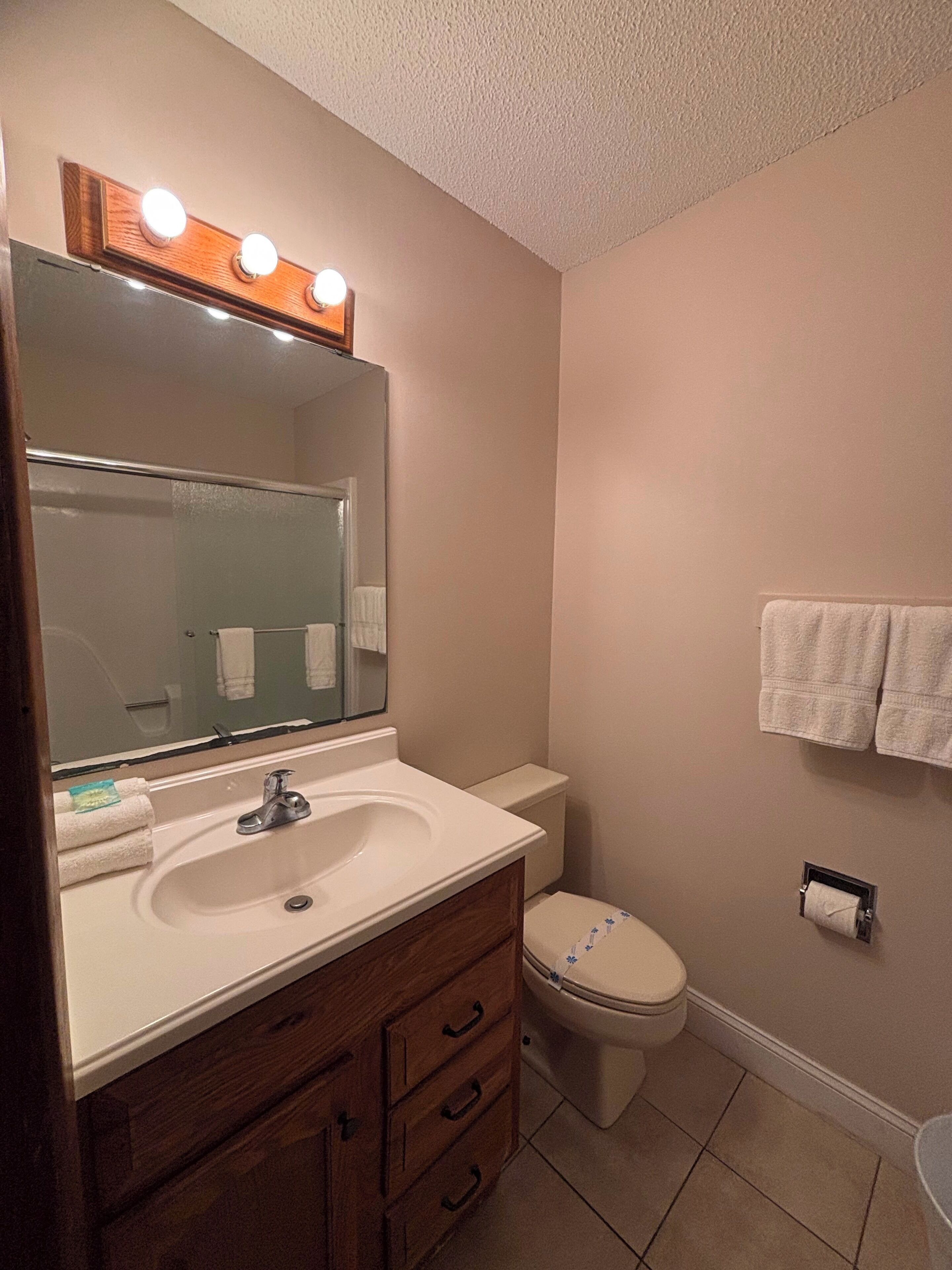A bathroom with a vanity, sink, mirror, and toilet.
