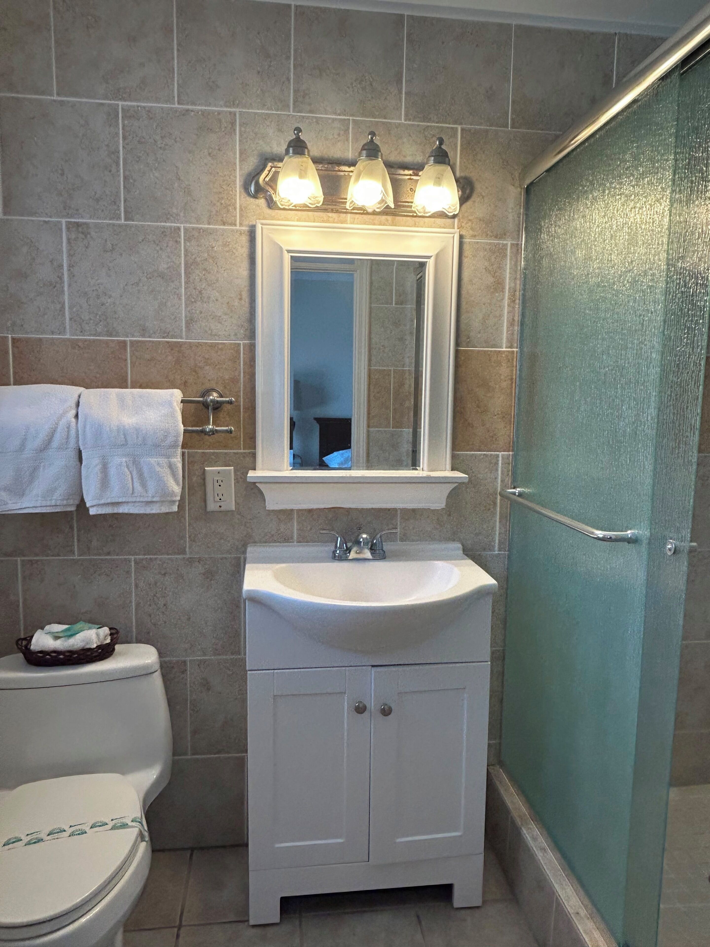 A bathroom with a white sink, a mirror above it, and a shower door.
