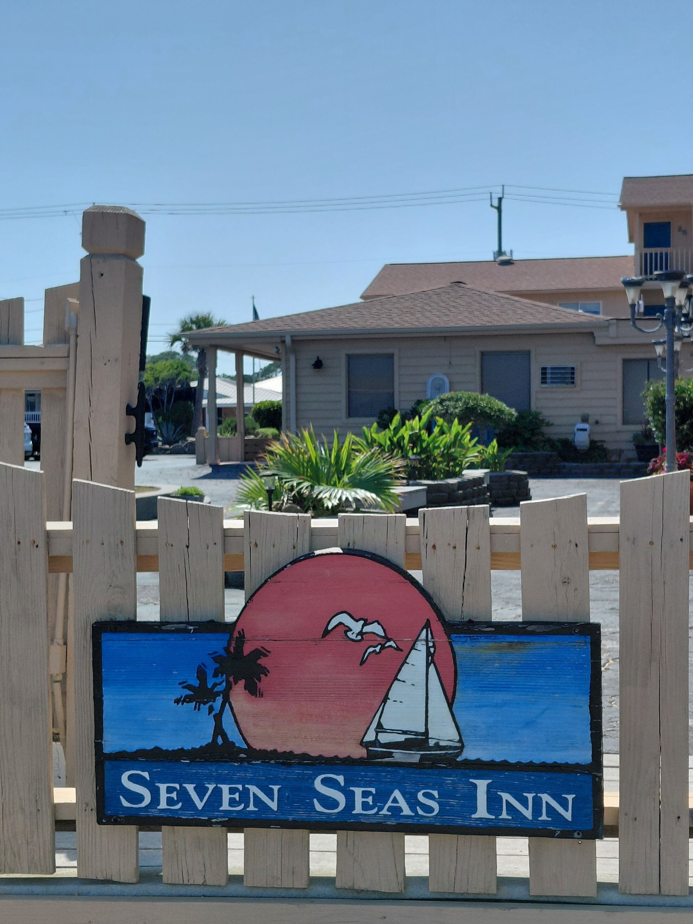 A wooden sign with a sailboat and palm tree, labeled 'Seven Seas Inn.'