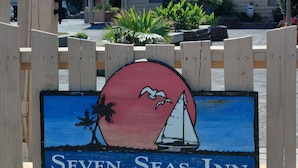 A wooden sign with a sailboat and palm tree, labeled 'Seven Seas Inn.'