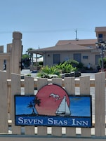 Uma placa de madeira com um veleiro e uma palmeira, com a inscrição 'Seven Seas Inn'.
