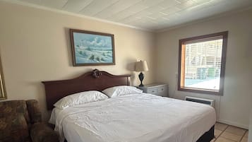 A hotel room with a bed, a chair, a nightstand, a lamp, a painting, and a window.