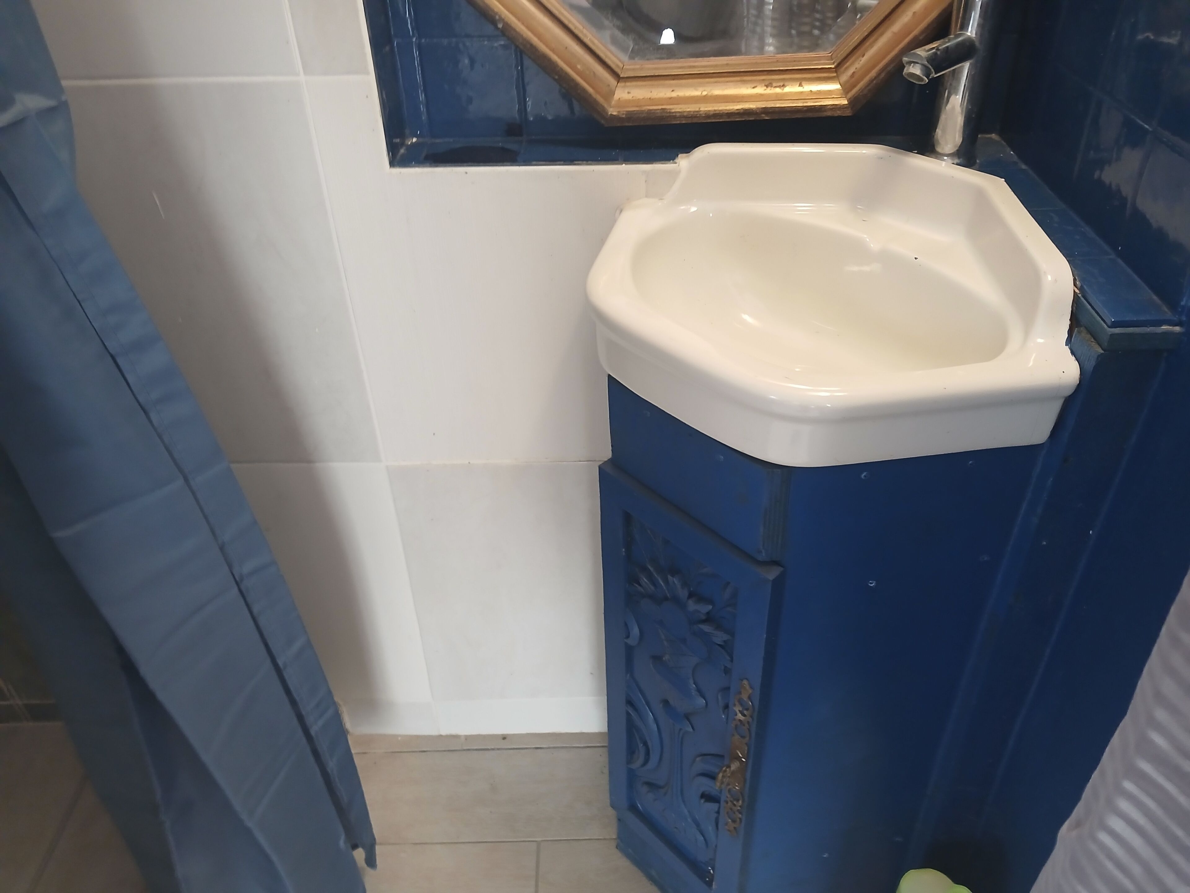 Een badkamer met een wit wastafel, blauwe kast en een spiegel met gouden lijst.