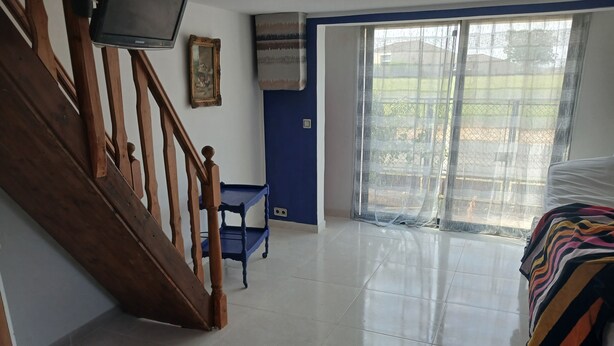 A room with a wooden staircase, a blue wall, a large window with a view, and a bed with a striped blanket. - Studio in a Charente-style house (Saint-Romain-de-Benet)
