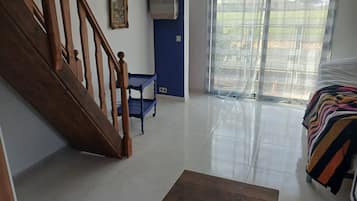 Een kamer met een houten trap, een blauwe muur, een groot raam met uitzicht en een bed met een gestreept dekbed.