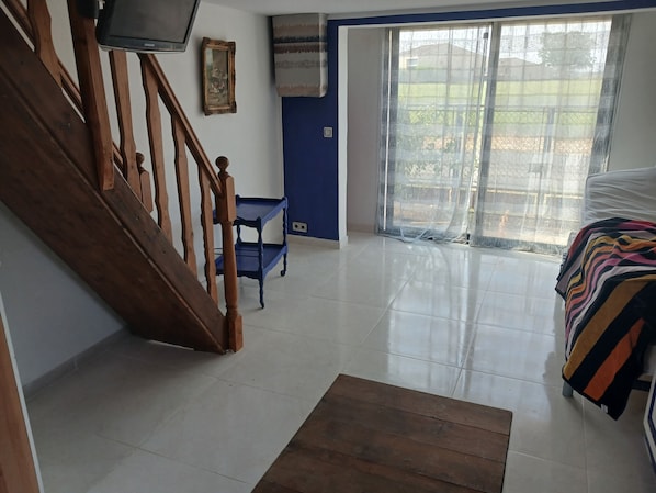 A room with a wooden staircase, a blue wall, a large window with a view, and a bed with a striped blanket.