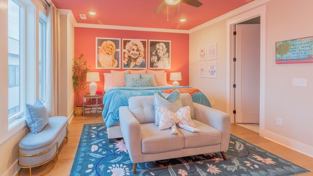 A bedroom with a bed, a chair, a ceiling fan, and a window. - Dolly's Pink Palace: Rooftop Deck (Nashville)
