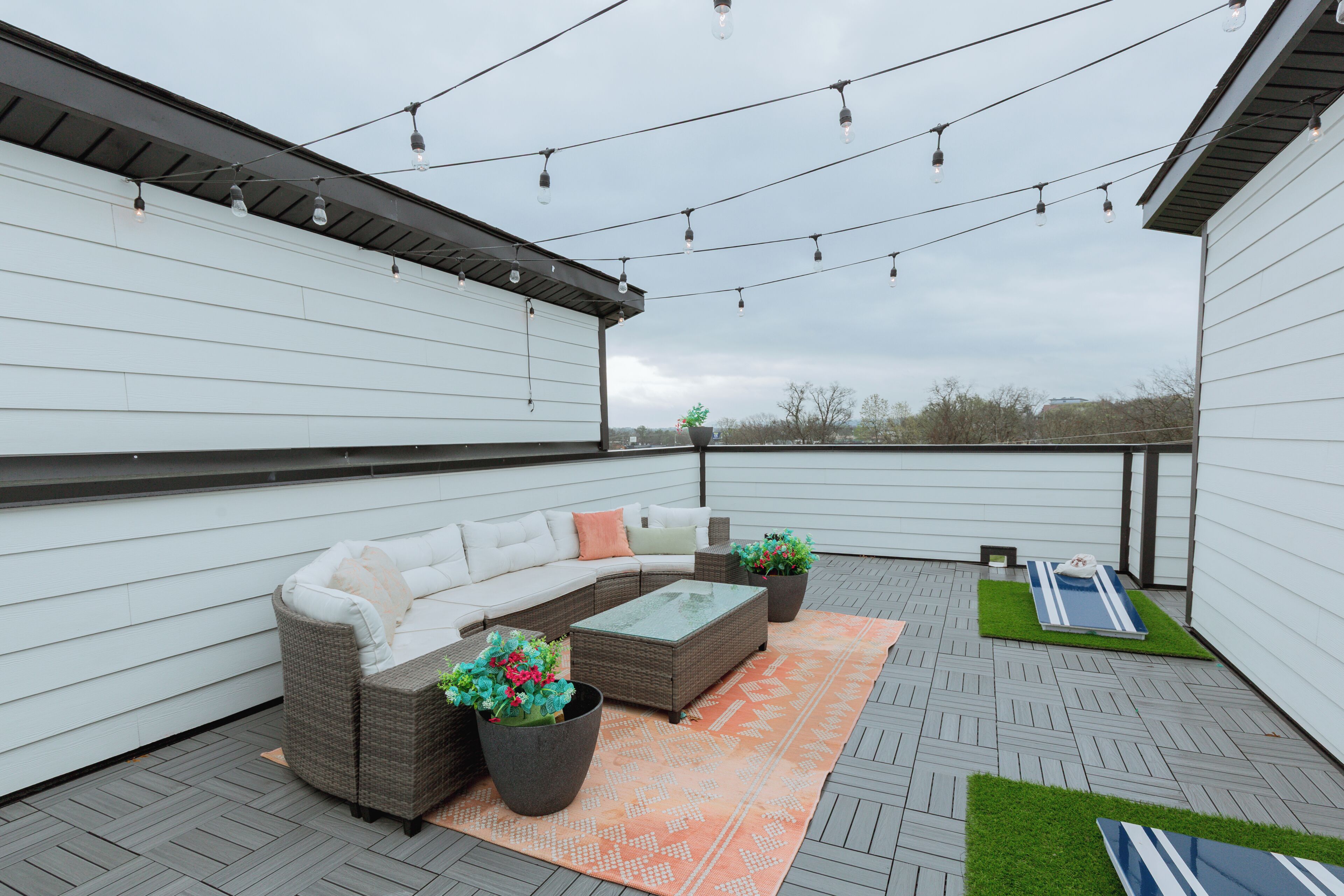 A covered patio with a sofa, coffee table, potted plants, and string lights.