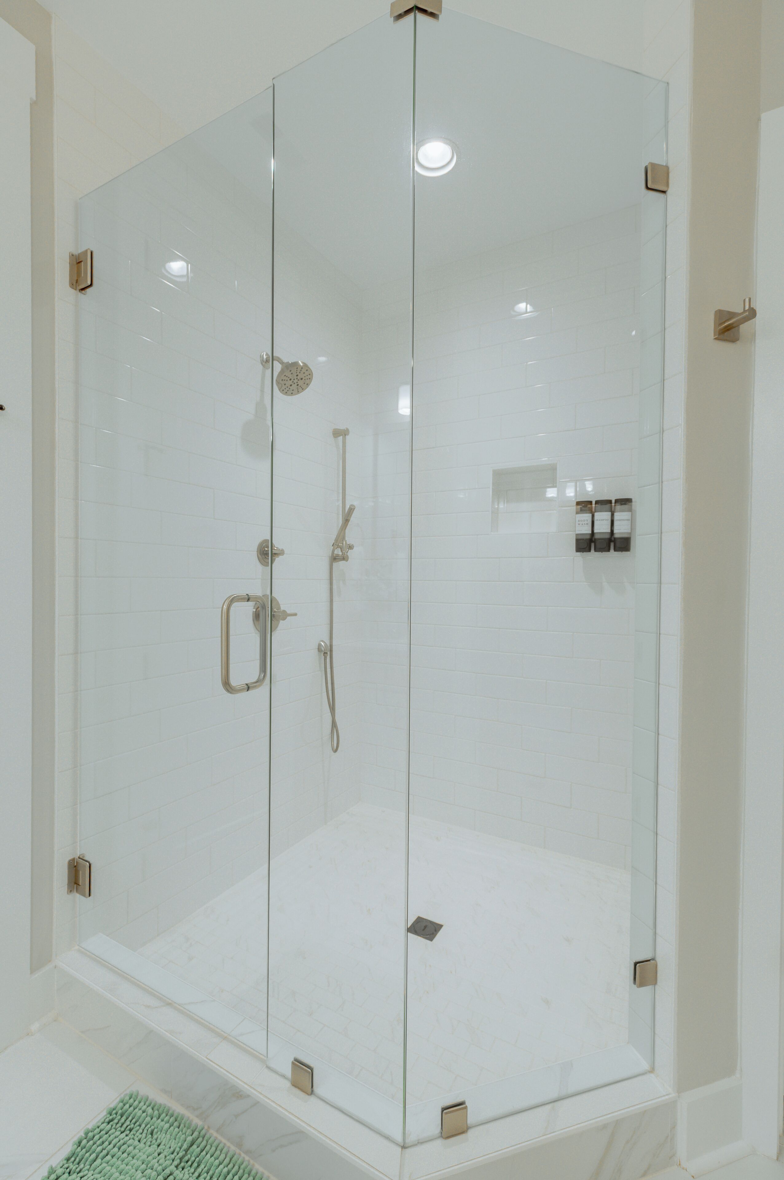 A glass-enclosed shower stall with a handheld showerhead, a handheld shower head, and a wall-mounted faucet.