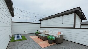 A covered outdoor patio with a sofa, potted plants, and string lights. - Dolly's Pink Palace: Rooftop Deck (Nashville)