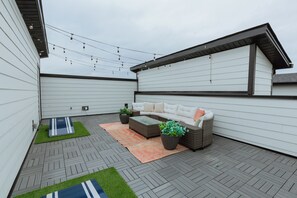 Eine überdachte Terrasse im Freien mit einer Couch, Topfpflanzen und Lichterketten.