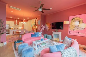 Sala de estar em tons de rosa, com um sofá, pufes, uma mesa de centro e uma lareira.