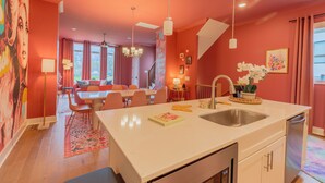 A modern kitchen with a central island, a dining area with a sofa and chairs, and a living room with a large painting on the wall. - Dolly's Pink Palace: Rooftop Deck (Nashville)
