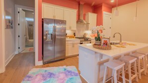 A modern kitchen with white cabinets, stainless steel appliances, and a central island with bar stools. - Dolly's Pink Palace: Rooftop Deck (Nashville)