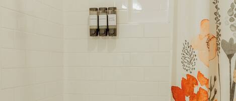 Un baño con ducha, bañera y retrete. Hay tres botellas de champú y acondicionador en la pared.
