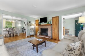 Ein Wohnzimmer mit Kamin, einer Couch, einem Couchtisch und einem Fernseher, der über dem Kamin angebracht ist.