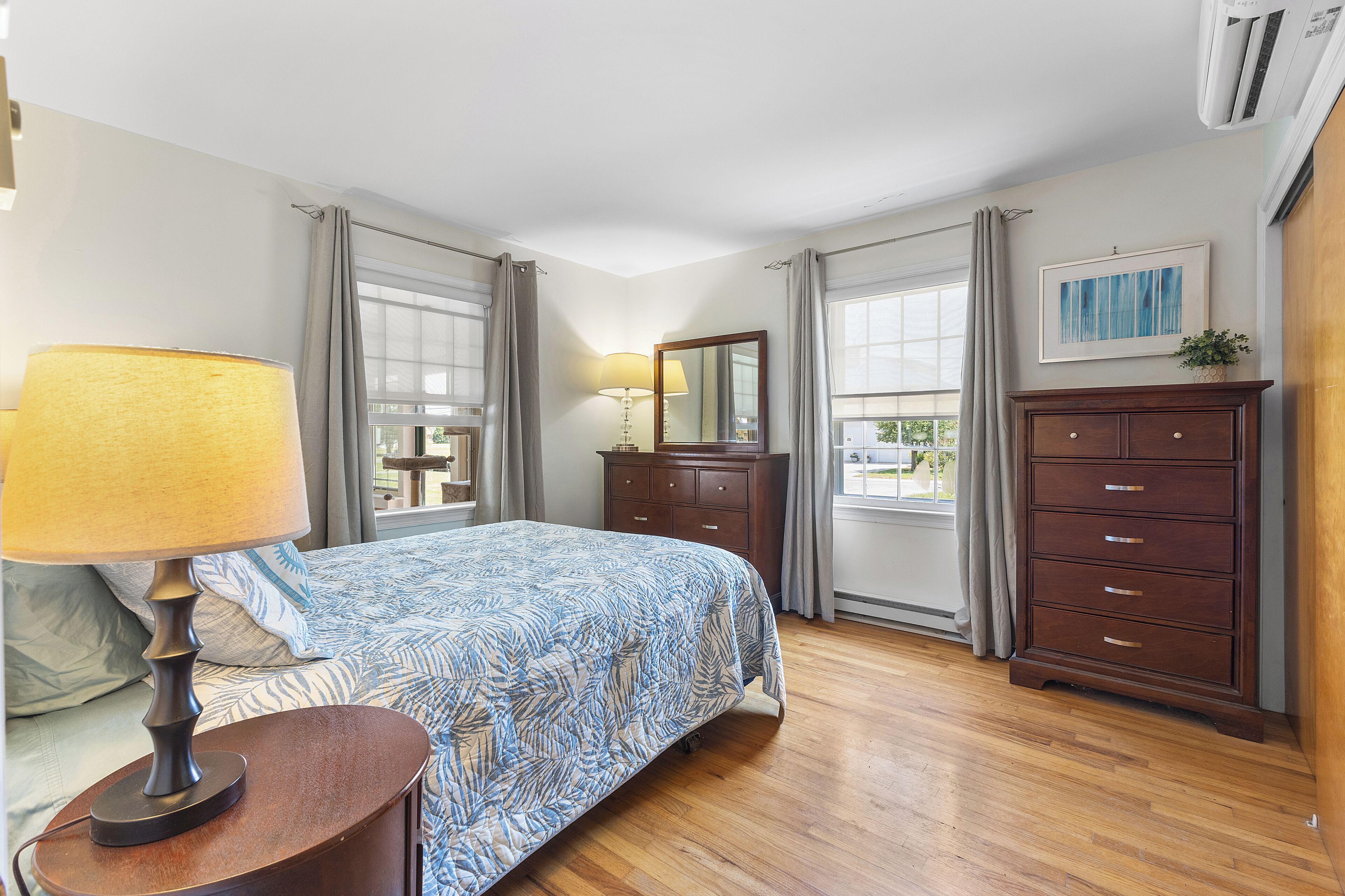 A bedroom with a bed, a dresser, a lamp, and a window with curtains.