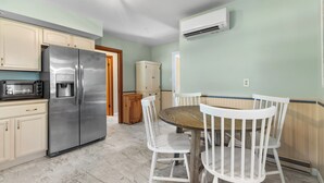 Une cuisine équipée d’un réfrigérateur en acier inoxydable, d’un four à micro-ondes, d’une table à manger en bois avec des chaises blanches et d’un meuble en bois.