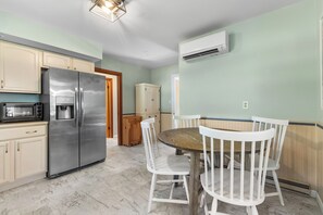 A kitchen with a stainless steel refrigerator, a microwave, a wooden dining table with white chairs, and a wooden cabinet.