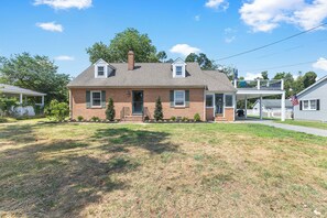 A two-story brick house with a front porch, a small front yard, and a visible American flag.