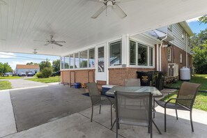 Eine überdachte Terrasse mit Tisch und Stühlen, einem Deckenventilator und einer Ziegelwand.