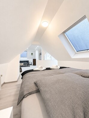 Ein modernes Schlafzimmer mit Dachfenster, einem Bett und Blick auf den Wohnbereich.