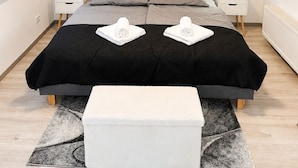 Um quarto moderno com teto inclinado, uma cama com colcha preta, duas mesas de cabeceira com abajures e um pequeno banco branco.