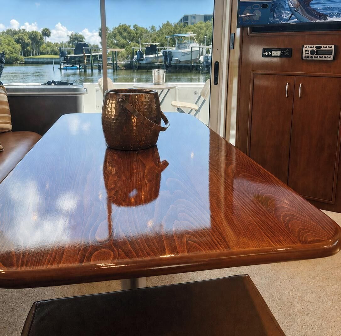 Ein Holztisch mit einem Metallbehälter darauf, eine gepolsterte Bank und Blick auf Boote durch ein Fenster.