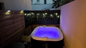 Ett bubbelbad med blått ljus, omgivet av en trävägg och en stenmur med växter.