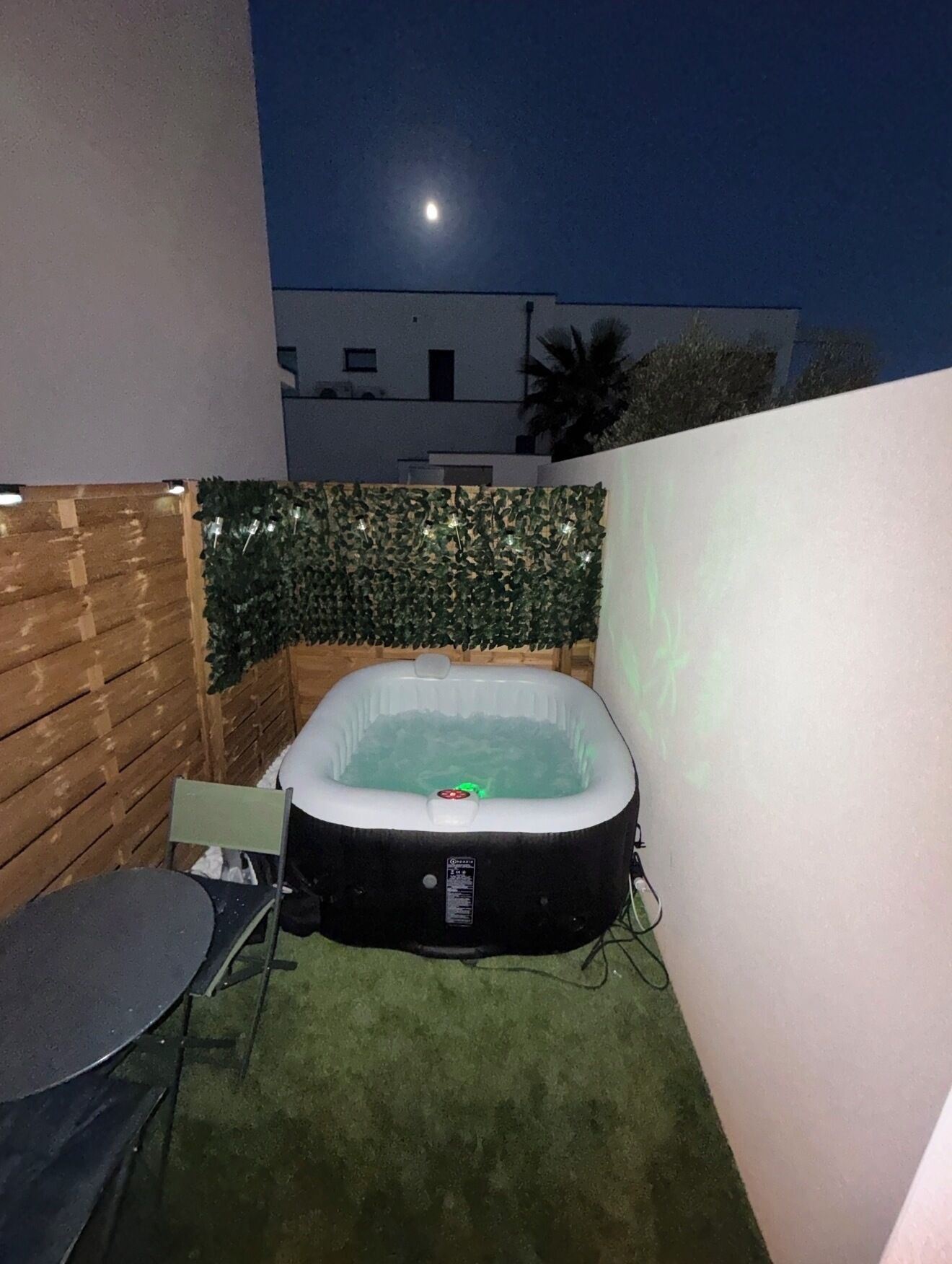 Un bain à remous installé dans un petit espace extérieur, agrémenté d’une clôture en bois et d’un mur.