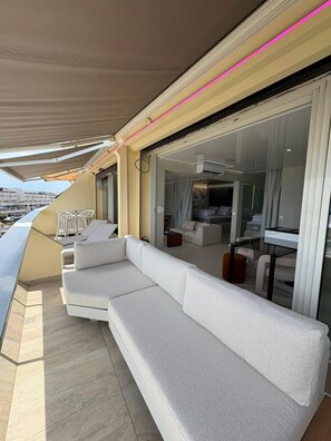 Ein Balkon mit einer weißen Couch, einem Glastisch und Blick auf die Stadt.