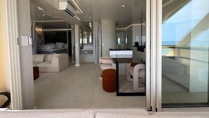 A modern hotel room with a glass wall, a sofa, a dining area, and a kitchen. - Spacious 3-Bedroom Apartment in a Naturist Village with Ocean Views (Agde)