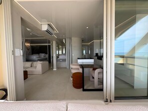 Ein modernes Hotelzimmer mit Glaswand, einer Couch, einem Essbereich und einer Küche.