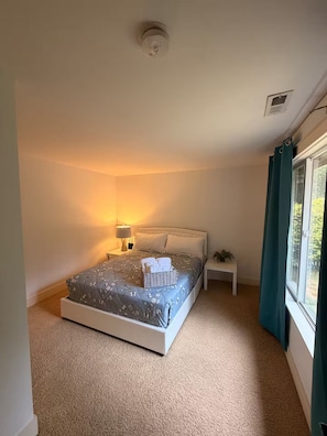 Ein Schlafzimmer mit Bett, Nachttisch, Lampe und einem Fenster mit Vorhängen.