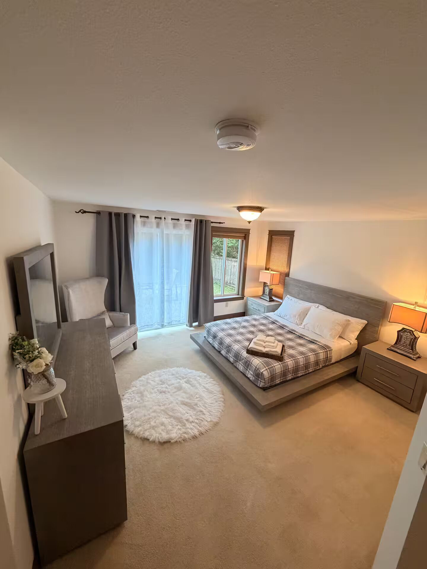 Ein Schlafzimmer mit einem Bett, Nachttischen, einem Sessel, einem kleinen Tisch mit einer Vase und einem runden Teppich.