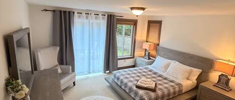 Ein Schlafzimmer mit einem Bett, Nachttischen, einem Sessel, einem kleinen Tisch mit einer Vase und einem runden Teppich.