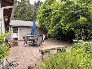 Eine Terrasse mit Tisch, Stühlen, einem blauen Sonnenschirm und einem Grill.