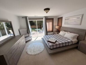 Ein Schlafzimmer mit einem Bett, einem Schminktisch, einem Stuhl, einer Lampe und Blick ins Freie.