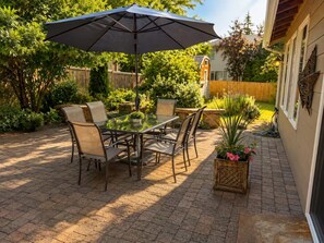 Eine Terrasse im Freien mit Tisch, Stühlen, einem großen Sonnenschirm und Pflanzen in Töpfen.