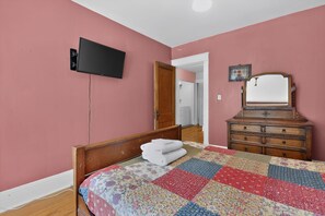 A bedroom with a bed, a dresser, a television, and a door leading to another room. - Widder Haus, 1909 Historic Home with Porches & BBQ (Kansas City)