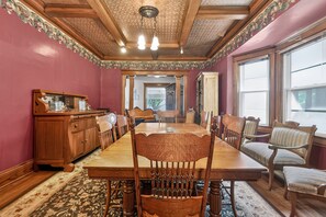 A dining room with a long wooden table, chairs, a wooden cabinet, and a patterned rug. - Widder Haus, 1909 Historic Home with Porches & BBQ (Kansas City)