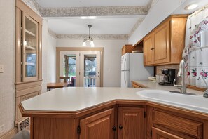 A kitchen with wooden cabinets, a white countertop, a refrigerator, and a window with a view of the outdoors. - Widder Haus, 1909 Historic Home with Porches & BBQ (Kansas City)