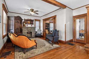 A traditional living room with a fireplace, wooden furniture, and a ceiling fan. - Widder Haus, 1909 Historic Home with Porches & BBQ (Kansas City)